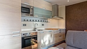 A modern kitchen with stainless steel appliances, wooden cabinets, and a grey sofa. - Apartamento con encanto en Barcelona&Playa (Badalona)