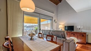A modern living room with a dining table, sofa, TV, and a view of the city through large windows. - Apartamento con encanto en Barcelona&Playa (Badalona)