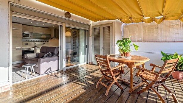 A wooden deck with a table and chairs, a sliding glass door leading to a kitchen, and a yellow canopy overhead. - Apartamento con encanto en Barcelona&Playa (Badalona)