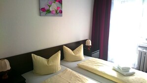 A hotel room with two beds, each with a pillow and a lamp. There is a painting on the wall and a window with curtains. - Ferienhotel Zwotatal (Klingenthal)