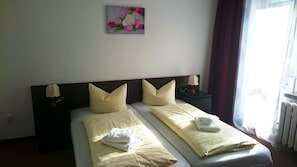 Habitación de hotel con dos camas, cada una con almohadas y toallas. Hay un cuadro en la pared sobre las camas, y una ventana con cortinas a la derecha.