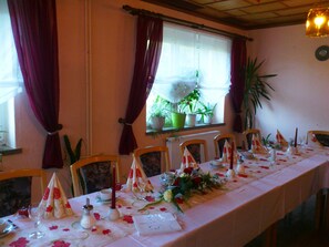 Una mesa puesta para una comida, con sillas, una ventana con cortinas, plantas en macetas y una planta en el alféizar.