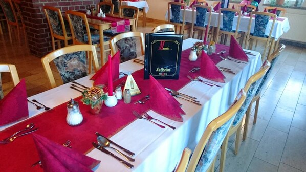A restaurant with tables set for dining, featuring a red tablecloth, silverware, and a bottle of Leikim.
