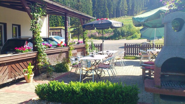An outdoor patio with tables and chairs, a barbecue grill, and a view of a forested area. - Ferienhotel Zwotatal (Klingenthal)