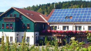 A building with a green facade and a white section with a balcony adorned with flowers. - Ferienhotel Zwotatal (Klingenthal)