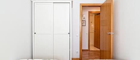 A small, clean room with two single beds, a white wardrobe, and a wooden door leading to another room.