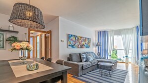 Ein modernes Wohnzimmer mit Essbereich, einem grauen Sofa, einem Streifenmuster-Teppich und einem großen abstrakten Gemälde an der Wand.