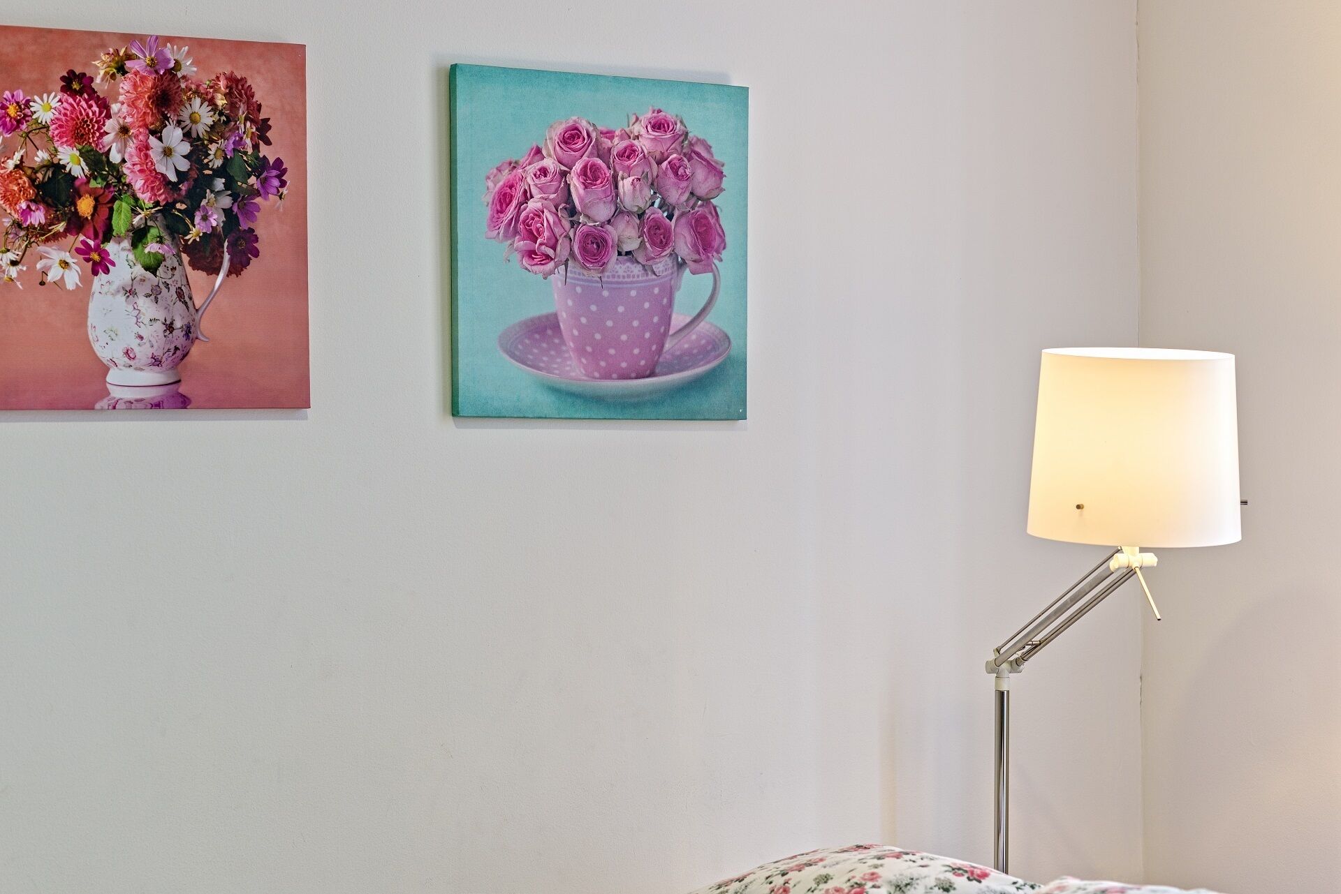 Een kamer met een bed, een lamp en twee bloemschilderijen aan de muur.
