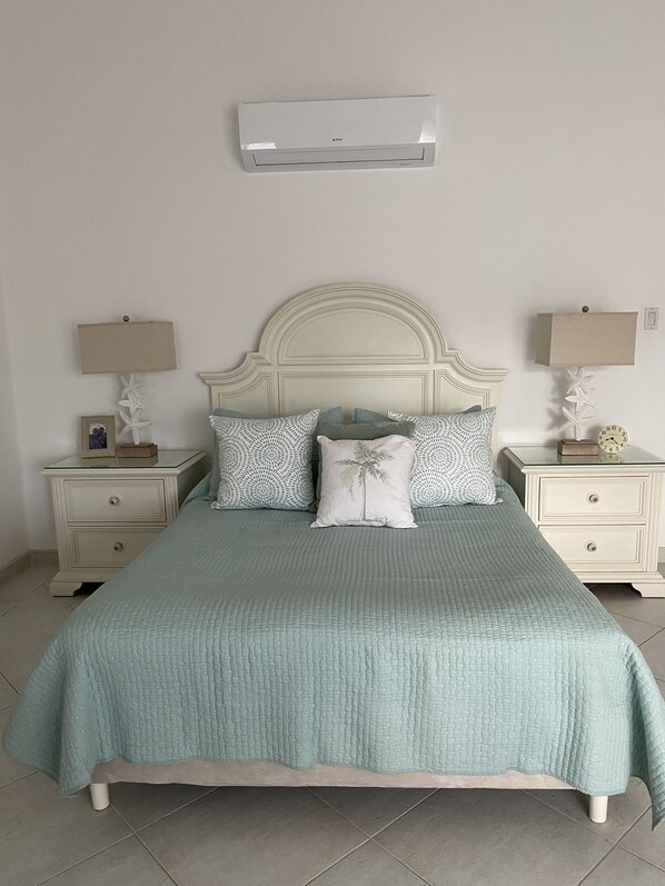 A bedroom with a bed, nightstands, a wall-mounted air conditioner, and a clock.