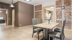 A dining area with a wooden table, four chairs, and a vase of white flowers. The walls have a brick pattern, and there is a clock on the wall. - WINWINSTAY Apartments Heart of Old Town (Riga)