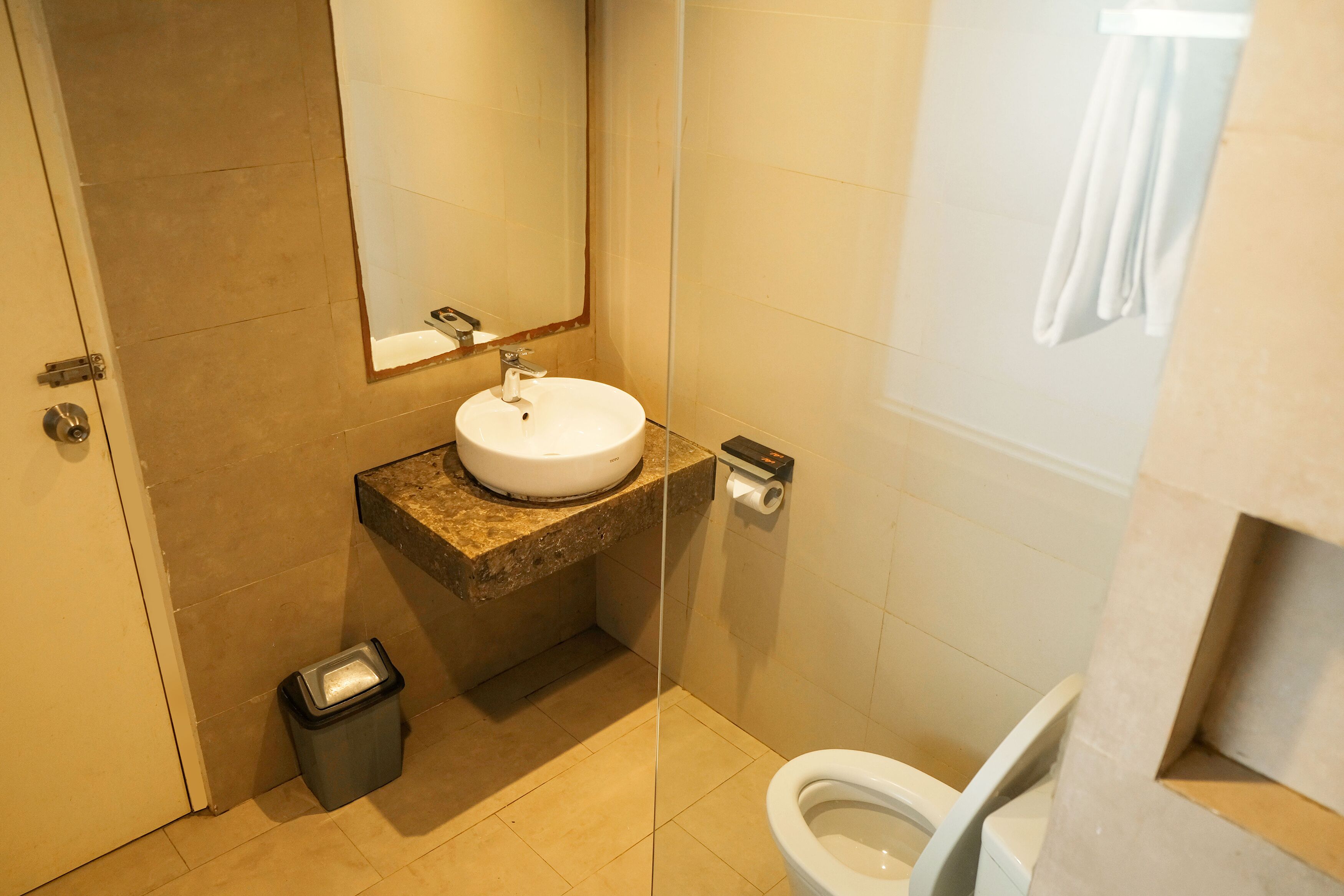 A modern bathroom with a sink, mirror, toilet, and trash bin.