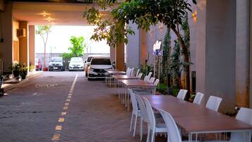 A covered outdoor dining area with tables and chairs, a white van parked in the background, and a 'DROP' sign on the ground.