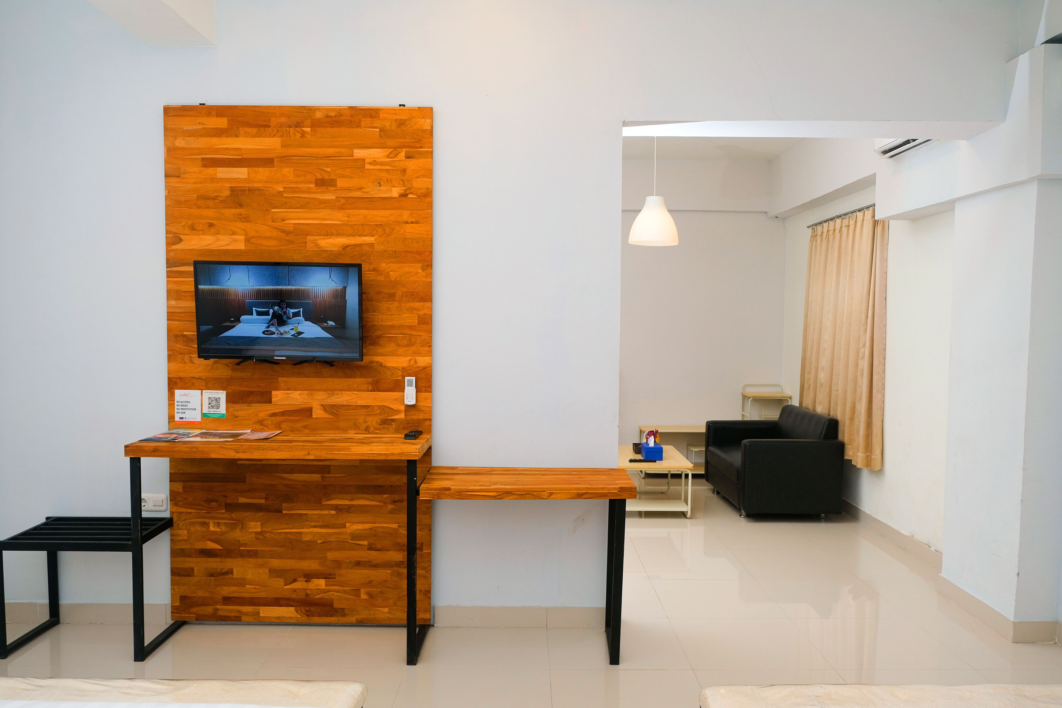 Un espace d’accueil moderne avec un mur en bois, un téléviseur fixé au mur, une petite table et un canapé en cuir noir.