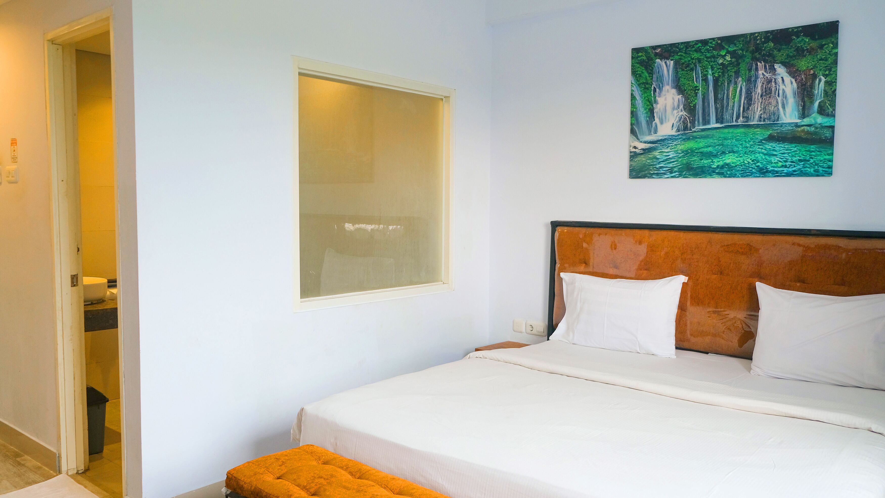 A bedroom with a bed, a window, and a painting of a waterfall.