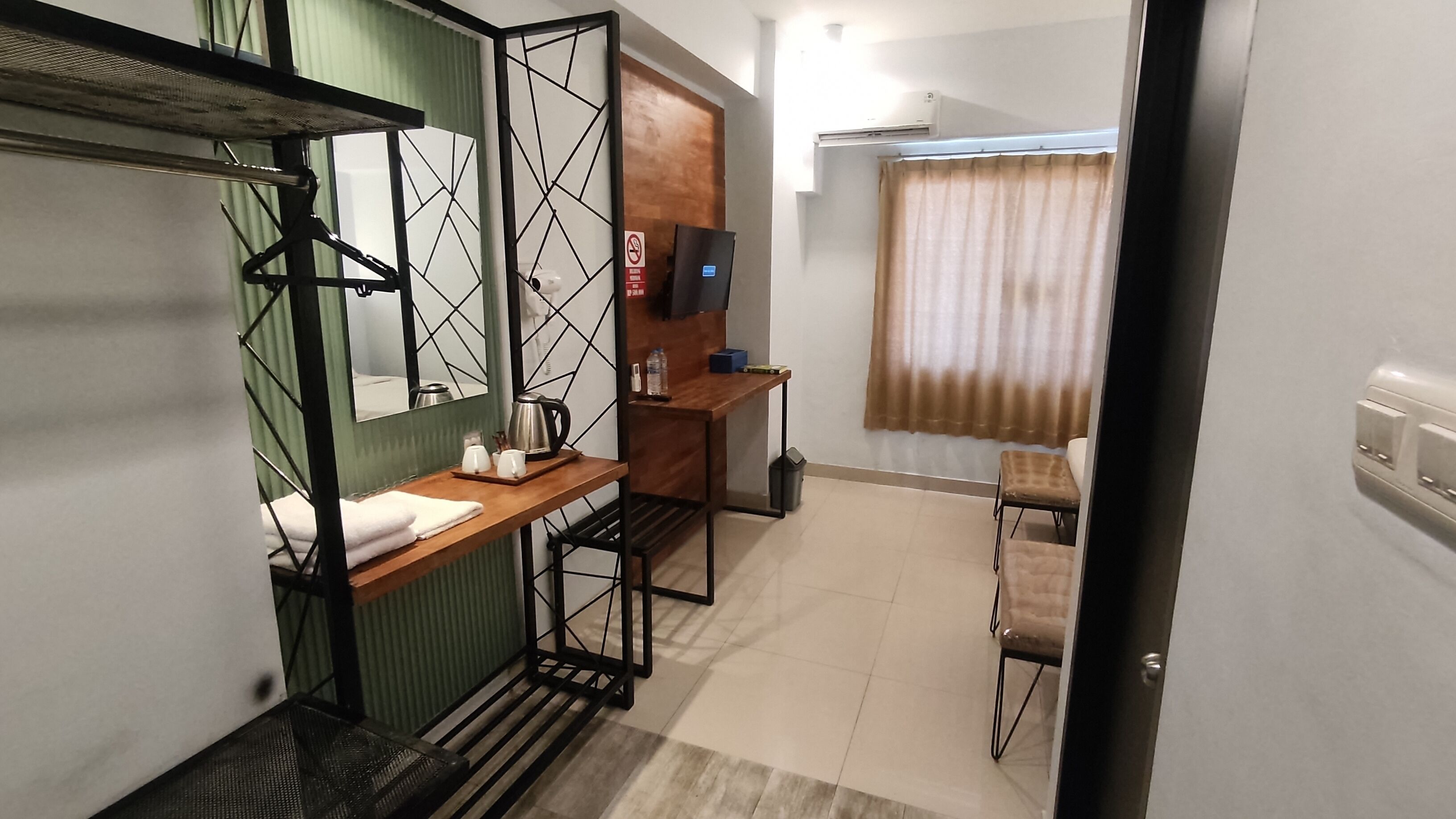 A compact hotel room with a bunk bed, a small desk with a chair, a television, and a window with curtains.