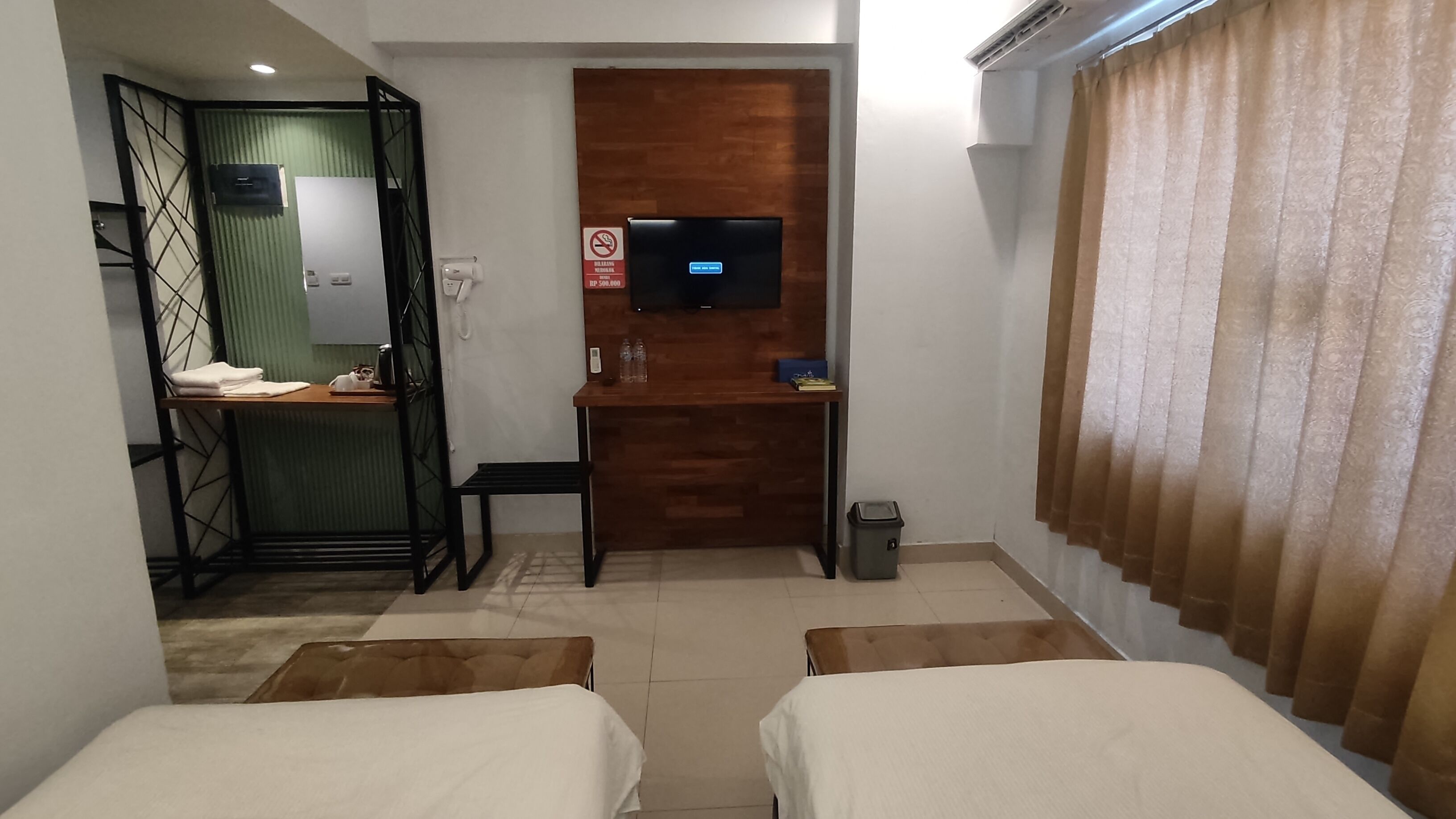 A hotel room with two beds, a desk with a TV, a small table, and a trash bin.