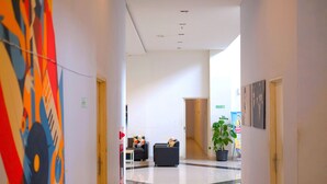 A modern hotel lobby with a clean, minimalist design, featuring a central seating area with two sofas and a potted plant.