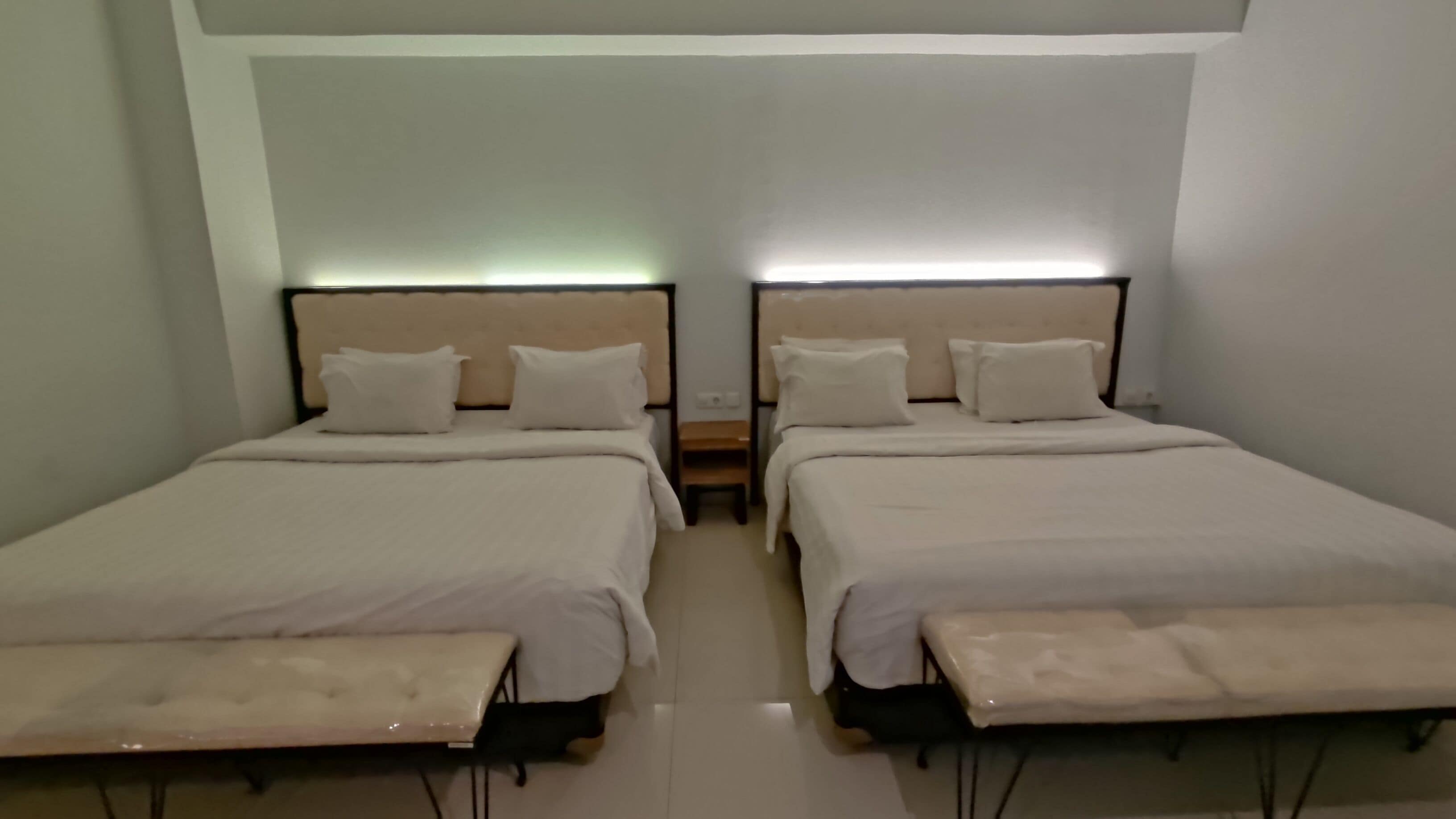 A twin room with two beds, each with a headboard, bedside tables, and a bench at the foot of the beds.