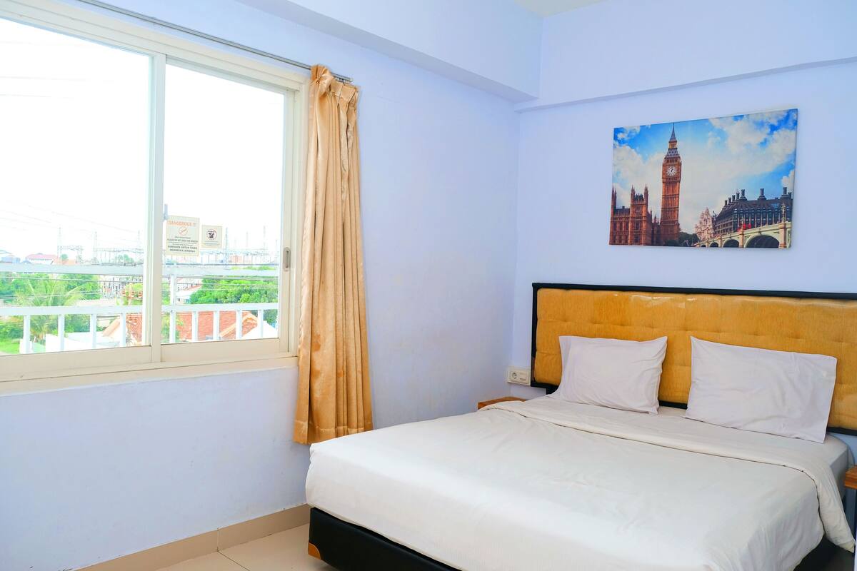 Een slaapkamer met een bed, een raam met gordijnen en een schilderij van een bekend monument.