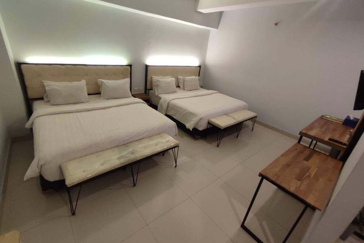 Een slaapkamer met twee bedden, een bankje en een klein houten tafeltje.