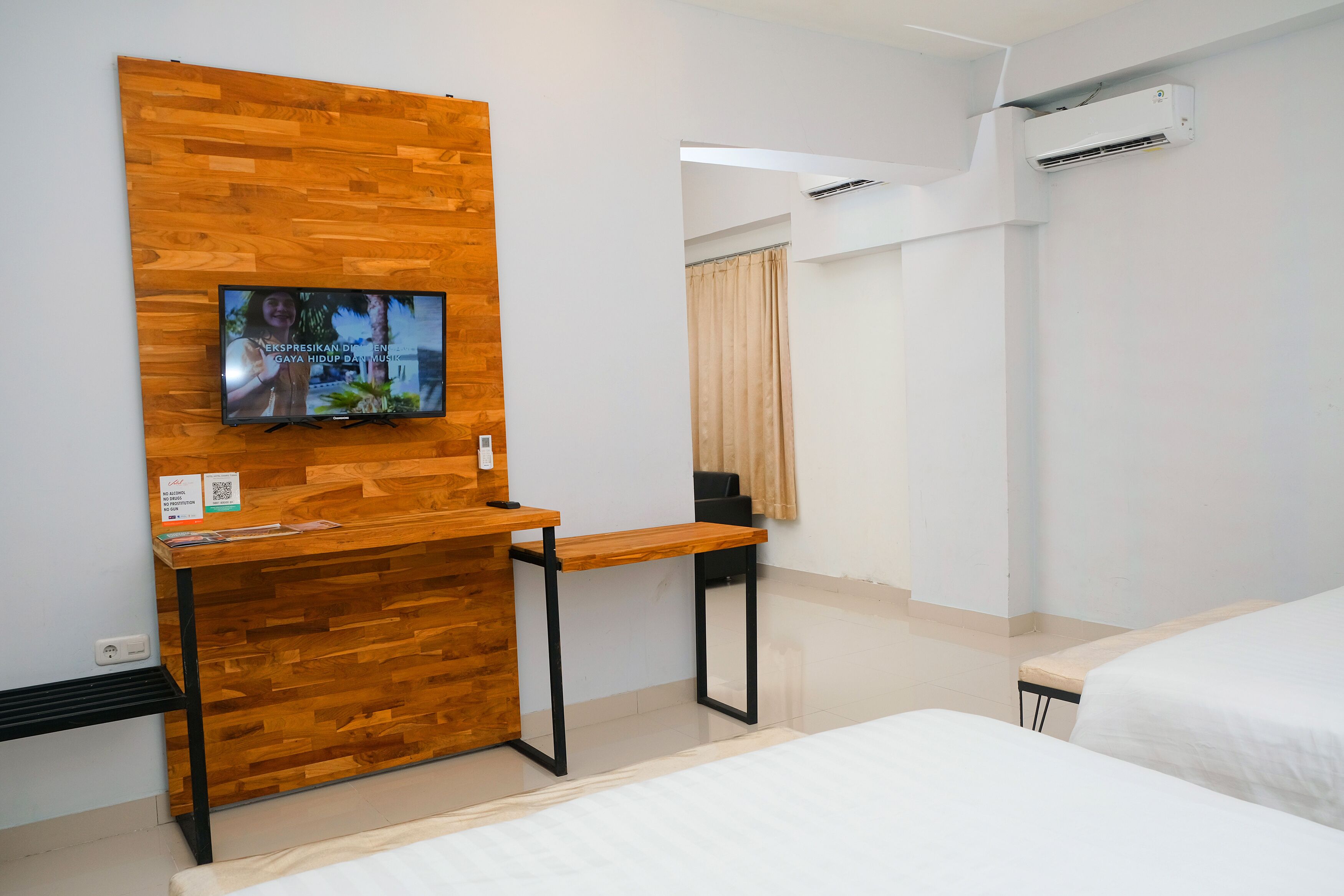 Habitación de hotel con un mostrador de recepción de madera, un televisor en la pared, una cama y un equipo de aire acondicionado.
