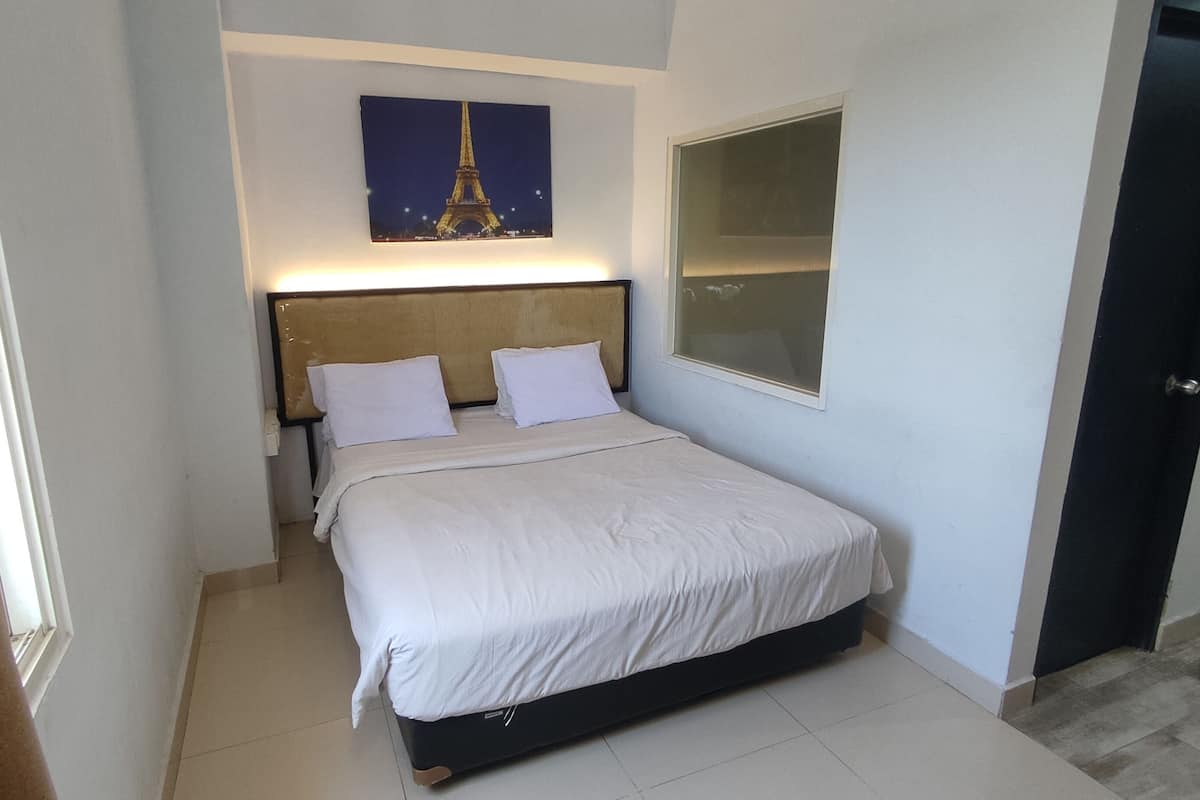 Een slaapkamer met een bed, een hoofdeinde, een nachtkastje, een aan de muur bevestigd plaatje van de Eiffeltoren, en een deur.