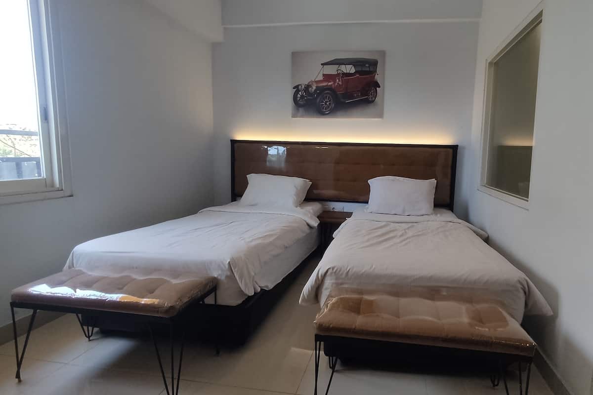Een kamer met twee eenpersoonsbedden, een houten hoofdbord, een ingelijst schilderij aan de muur en een raam aan de linkerkant.