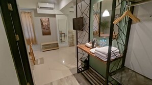 A modern hotel room with a wooden bench, a small table with toiletries, a hanging towel rack, and a view of the city through a window.
