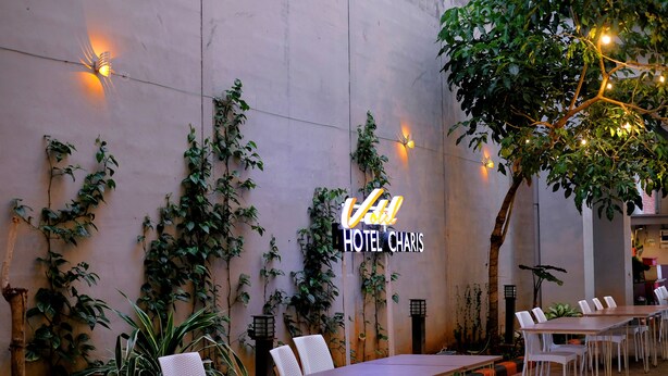 An outdoor seating area with tables and chairs, a wall with climbing plants, and a sign for Hotel Charis.