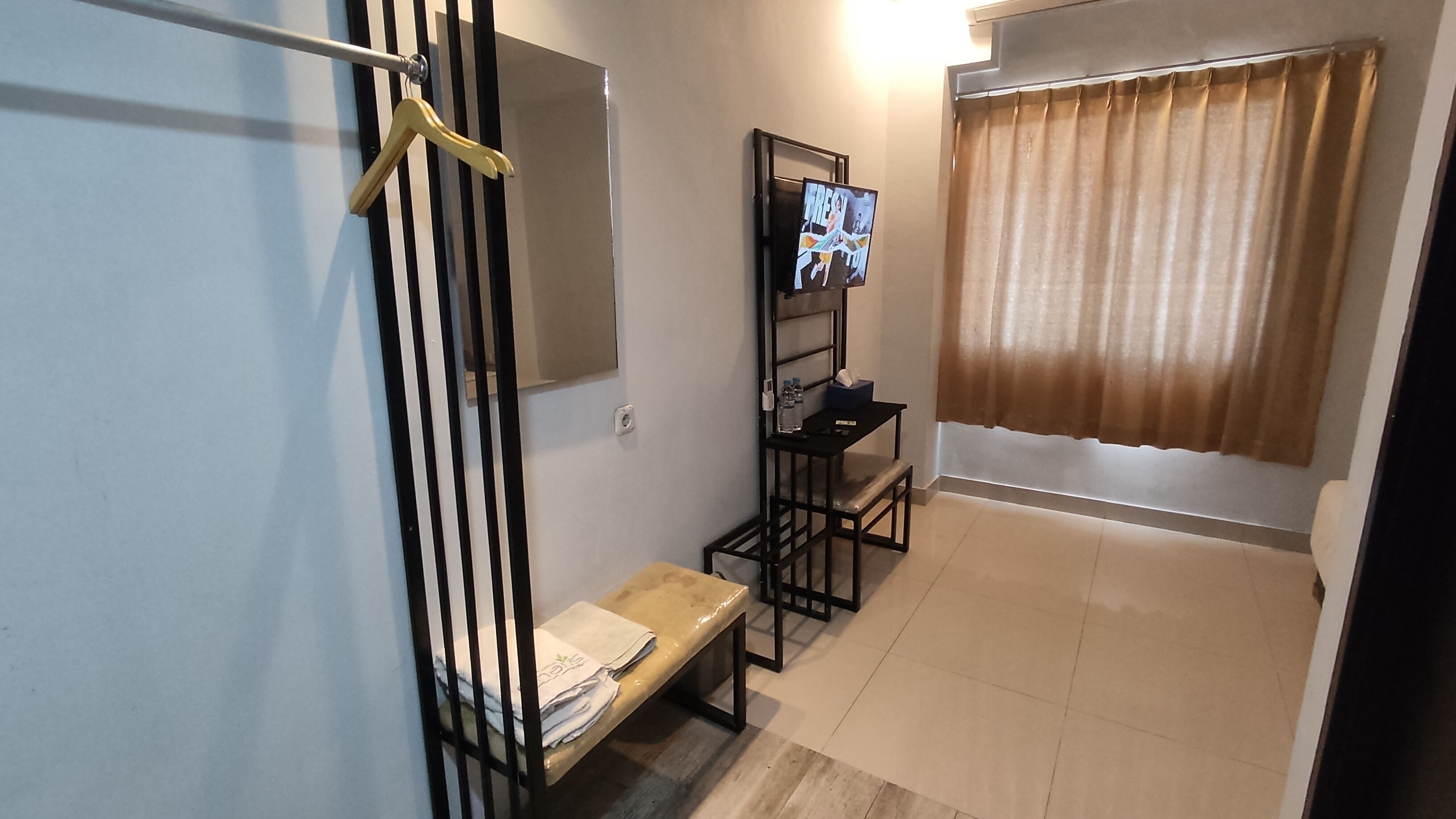 A small, compact room with a bench, a shelf with personal items, a mirror, and a window with curtains.