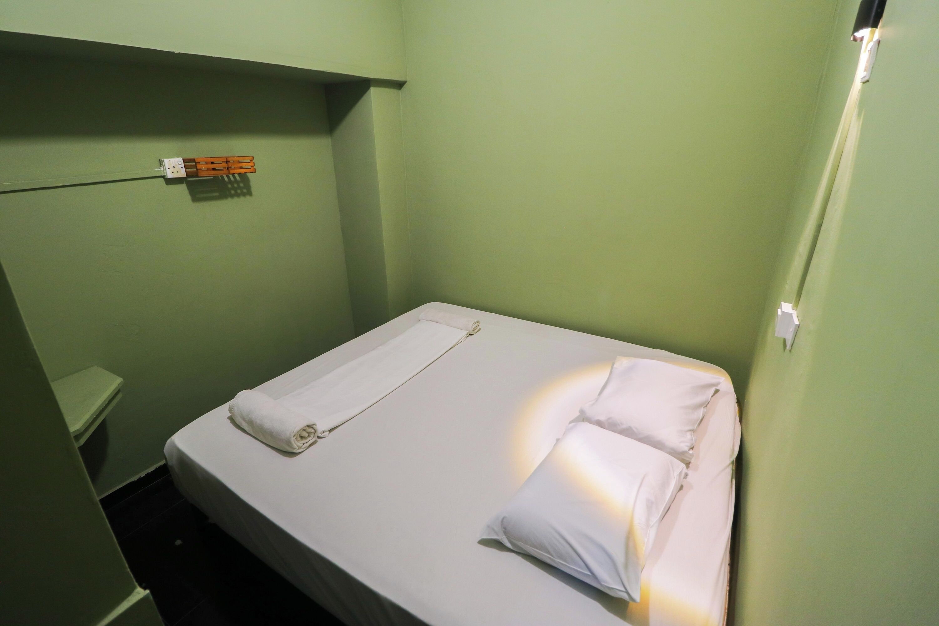 A small, single-bed room with a green wall, a white bedspread, and a white pillow.