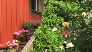 Un escalier en bois mène à un porche orné d’un mur rouge, de plantes en pot et de différentes variétés de fleurs.