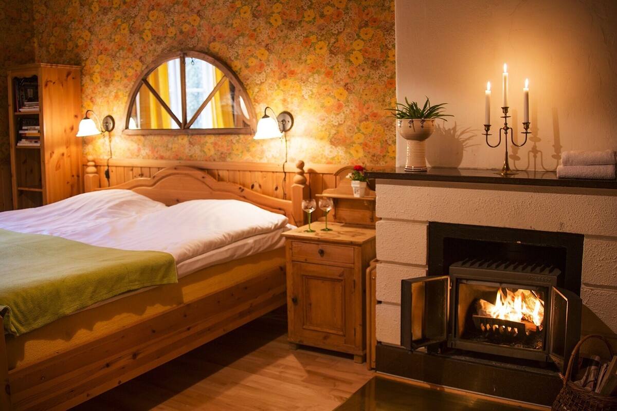 Un dormitorio acogedor con cama de madera, chimenea y papel tapiz floral.