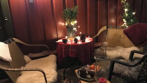 Un espace extérieur accueillant, aménagé avec des chaises en osier et une table pour deux, agrémenté d’une nappe rouge et de bougies.