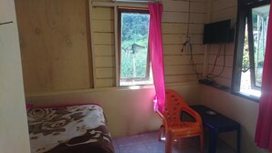 A room with a bed, a window with a curtain, a television mounted on the wall, and a small table.