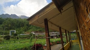 A covered outdoor area with a view of mountains, a small building, and a gate.