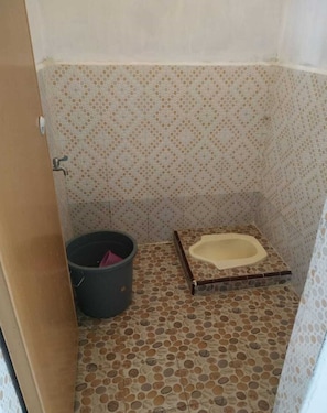 Een kleine betegelde badkamer met een toilet, een emmer en een deur.