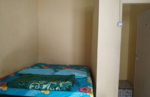 Een kleine kamer met een enkel bed, een bedspreide met bloemenprint en een groen kussen.