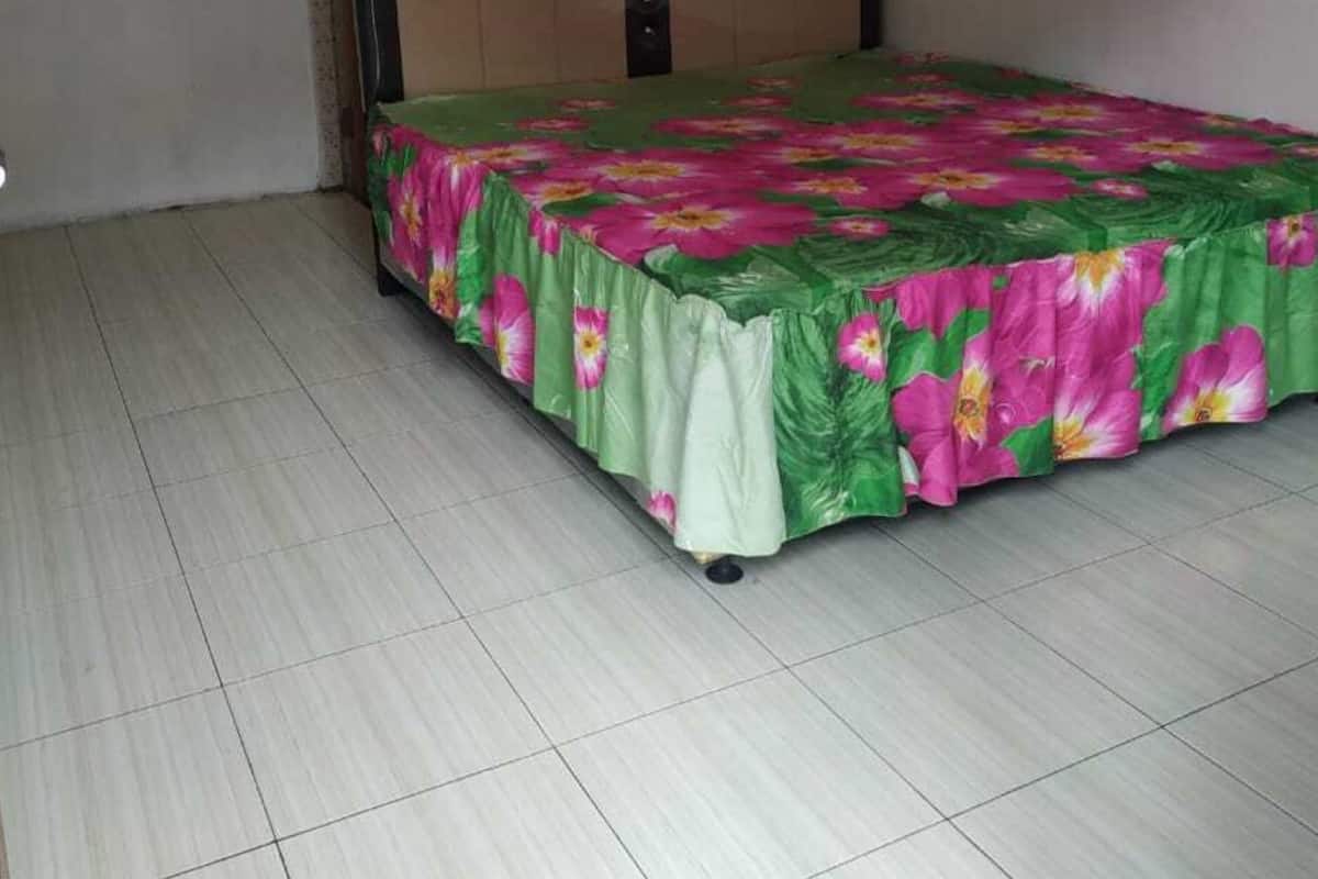 A room with a bed, plain walls, and tiled flooring.