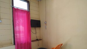 A small room with a pink curtain, a television mounted on the wall, a bench, and an orange chair.