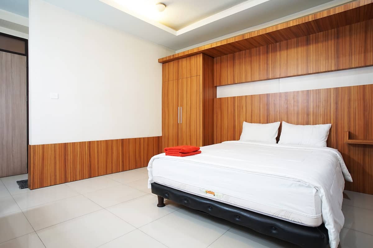 A modern bedroom with a large bed, wooden paneling, and a white ceiling light.
