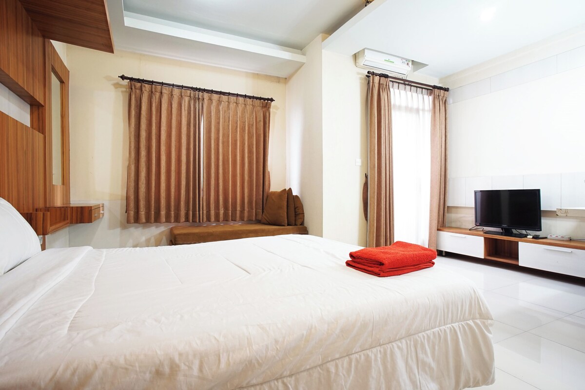 A hotel room with a bed, a TV, and a window with curtains.