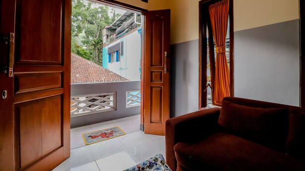 Una habitació amb una porta de fusta, un sofà marró i vista cap a un edifici blau per una porta oberta.