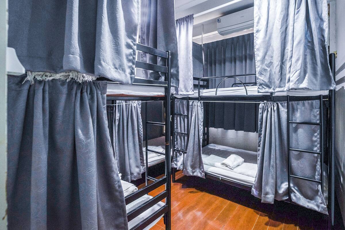 A dormitory room with bunk beds, grey curtains, and a wooden floor.