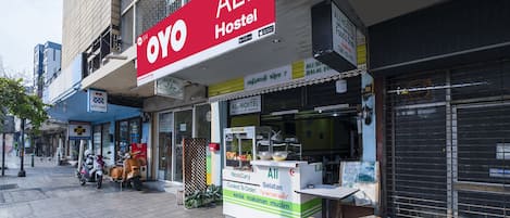 A hostel with a prominent red sign, a small outdoor seating area, and a closed shutter on the right.