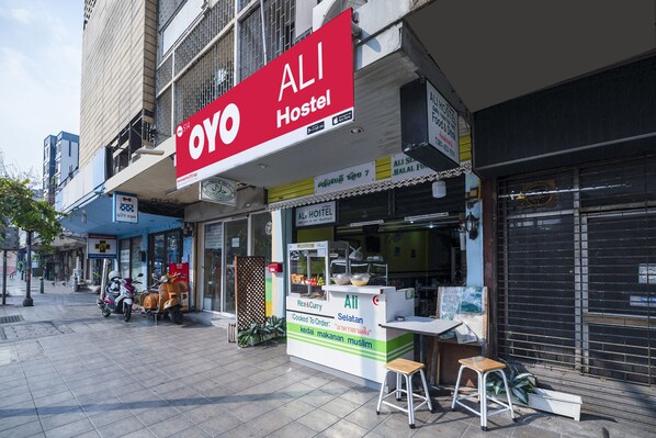 A hostel with a prominent red sign, a small outdoor seating area, and a closed shutter on the right.