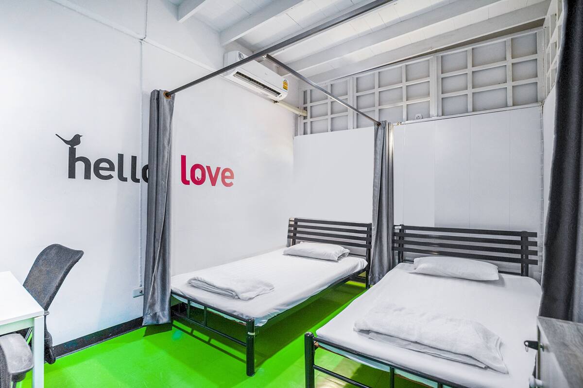 A room with two beds, a desk, and a 'hello love' sign on the wall.