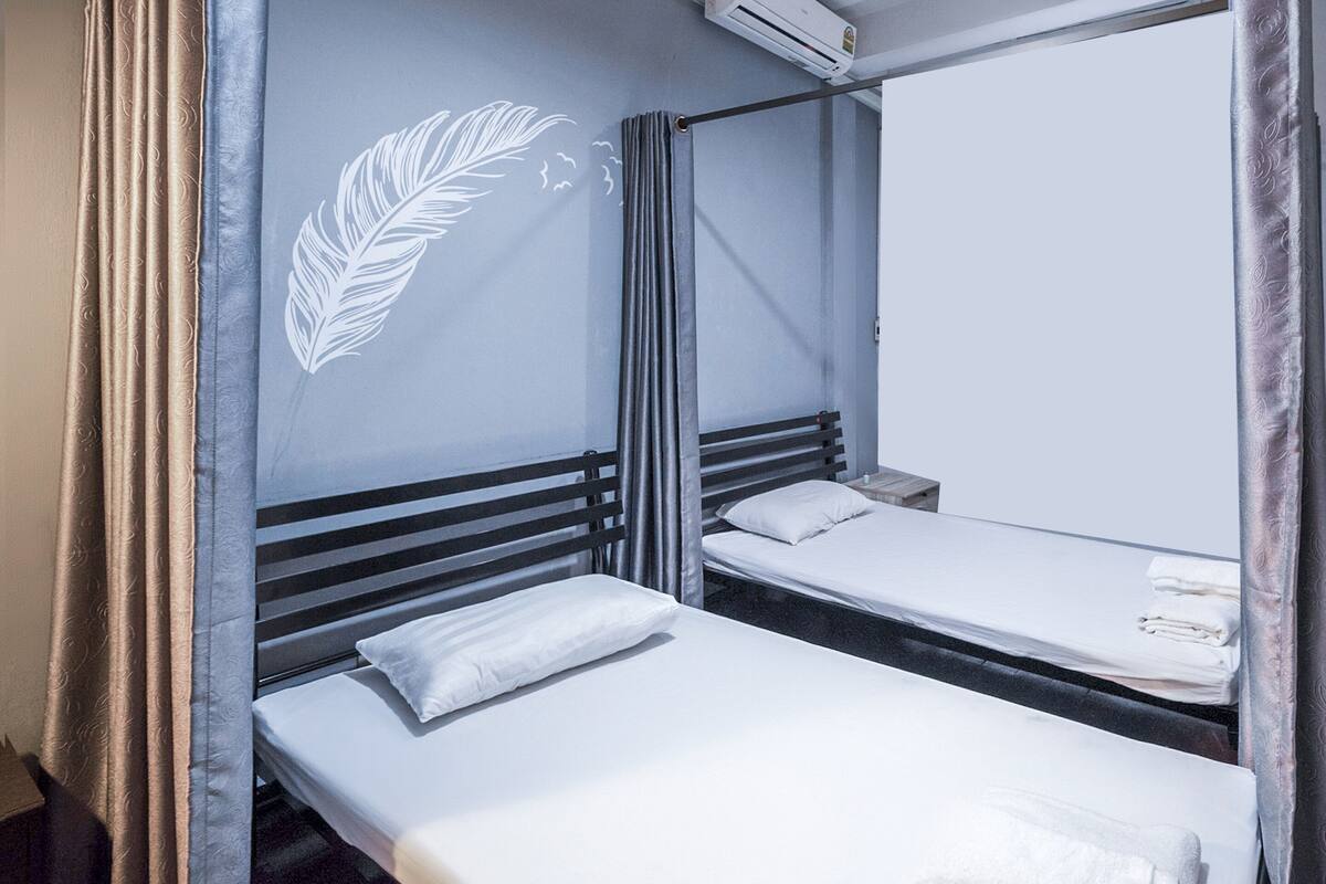 A room with two single beds, a headboard with a leaf design, and a window with curtains.