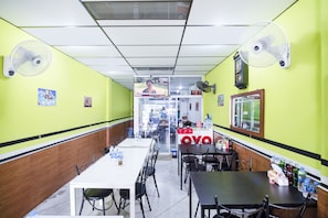 A restaurant with tables and chairs, a reception desk, and wall-mounted fans. - OYO 514 Ali Hostel (Bangkok)