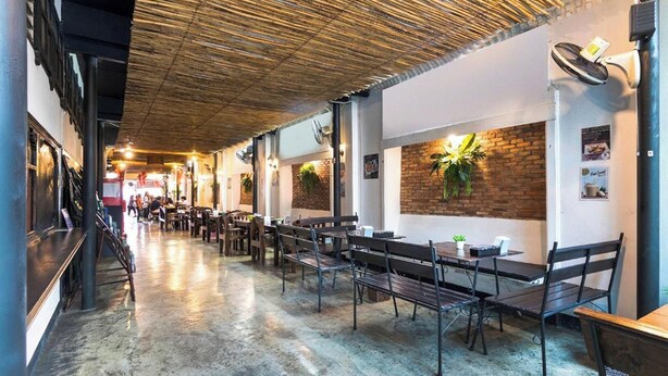 A spacious indoor dining area with long tables and benches, brick walls, and hanging plants. - Baan Lanna At Phrasingh (Chiang Mai)